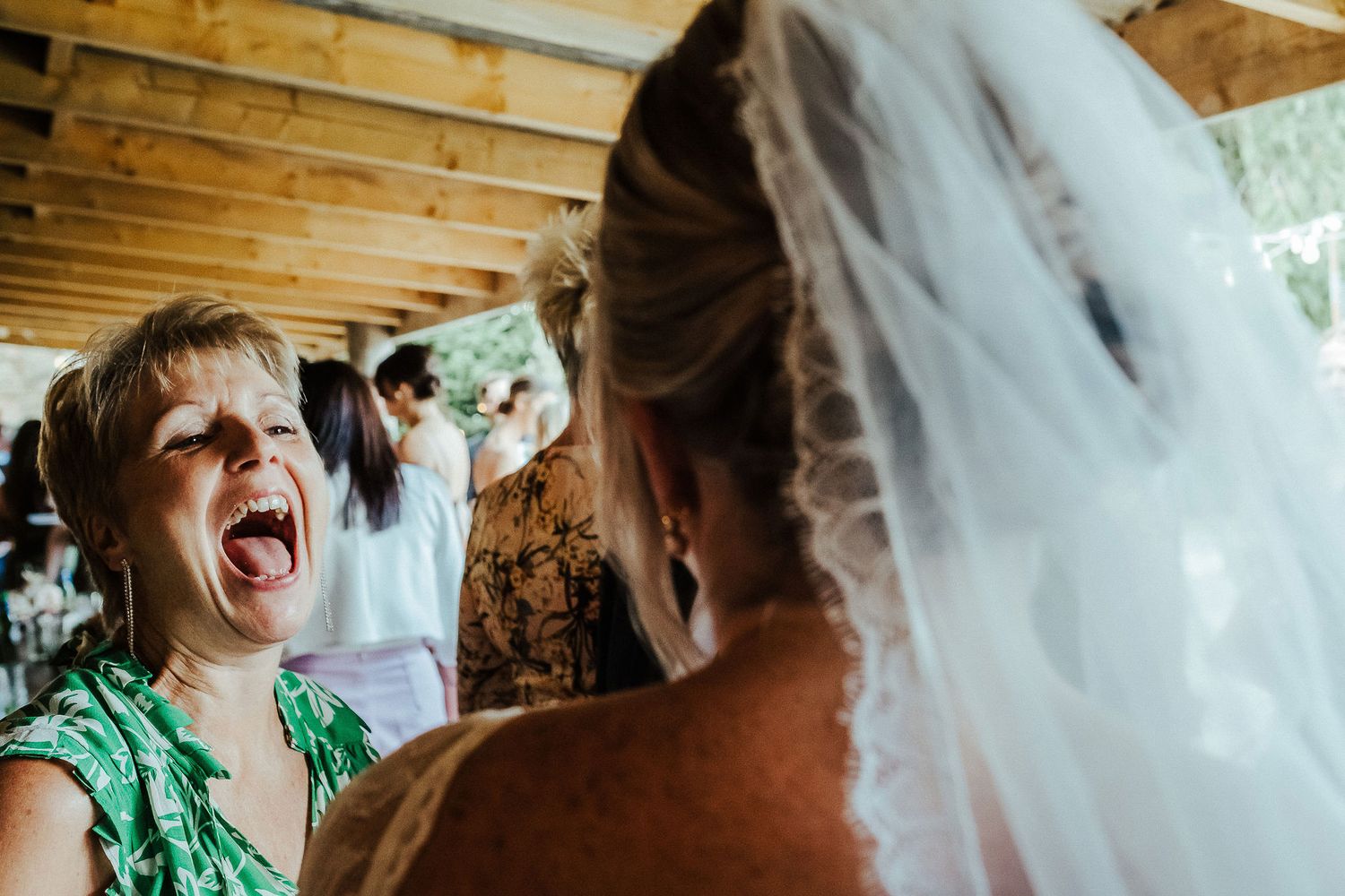 Young wedding guest reacts with excitement while talking to the bride at an outdoor venue.