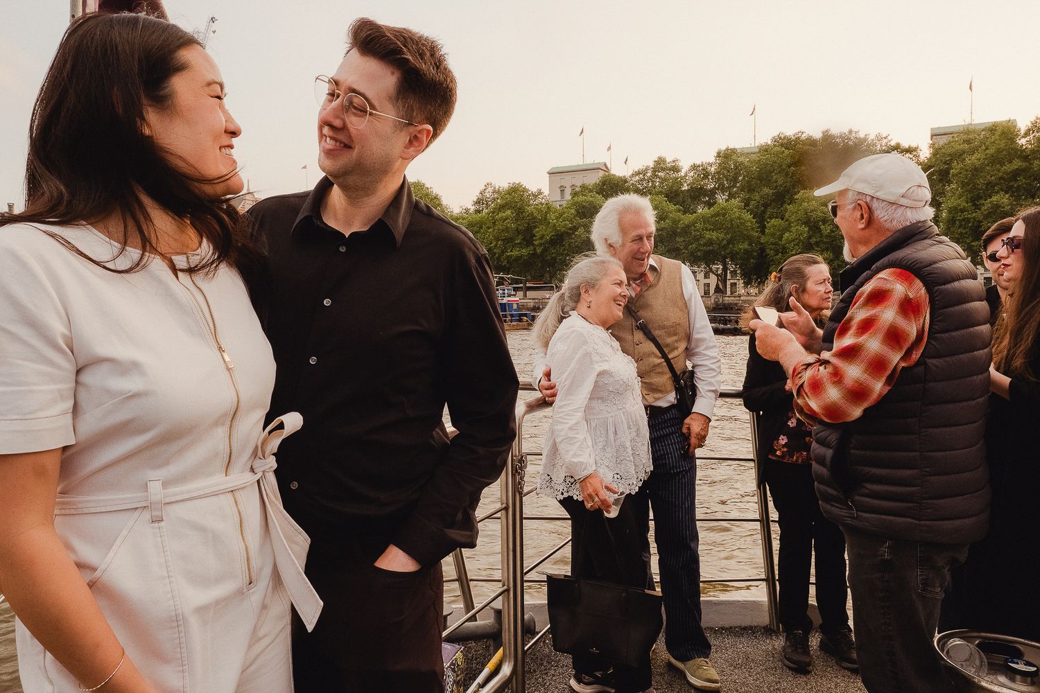 Group of people socializing on a boat deck during sunset with casual and plaid attire.