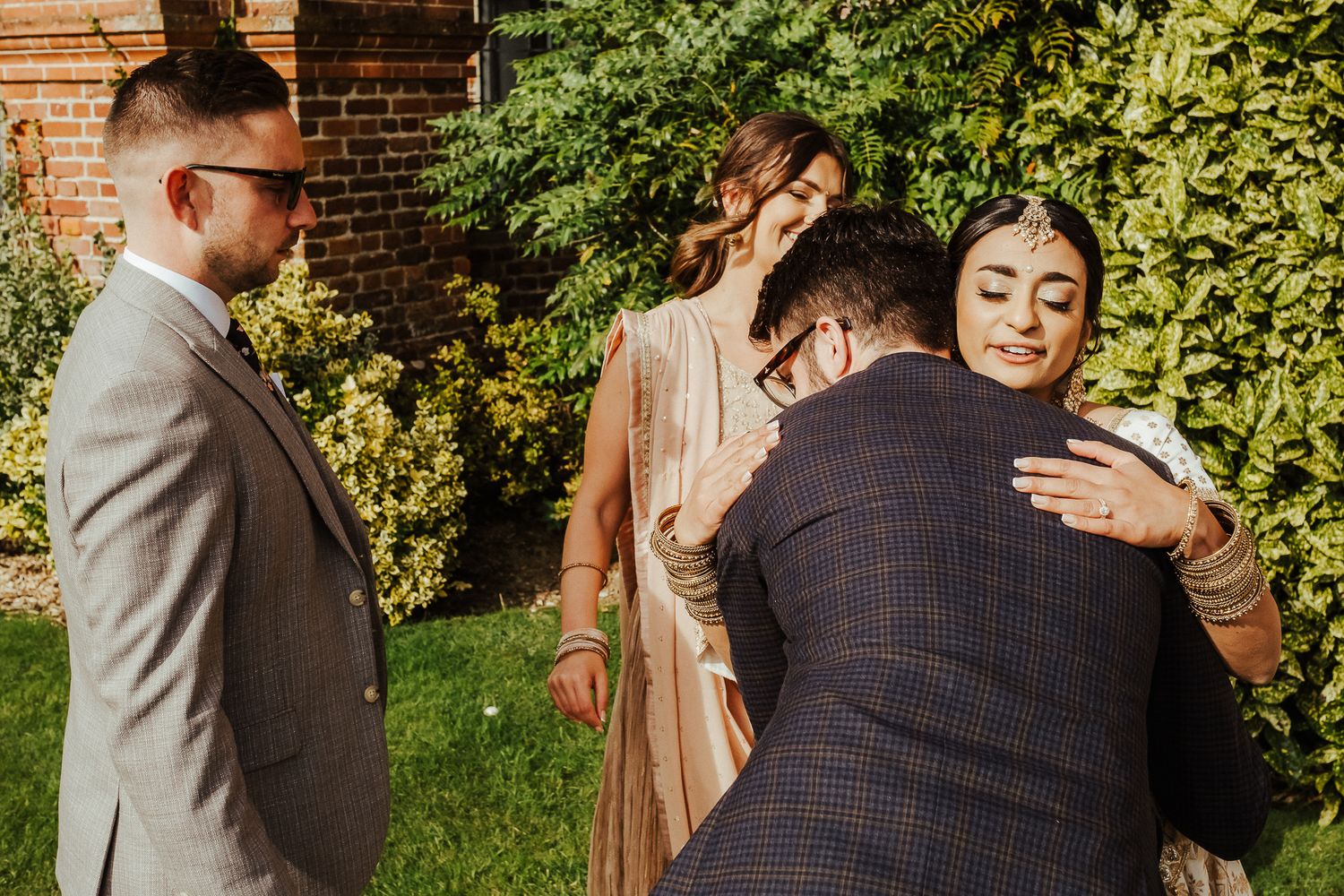 A romantic moment between two people embracing outdoors beside a brick wall in an elegant wedding setting.