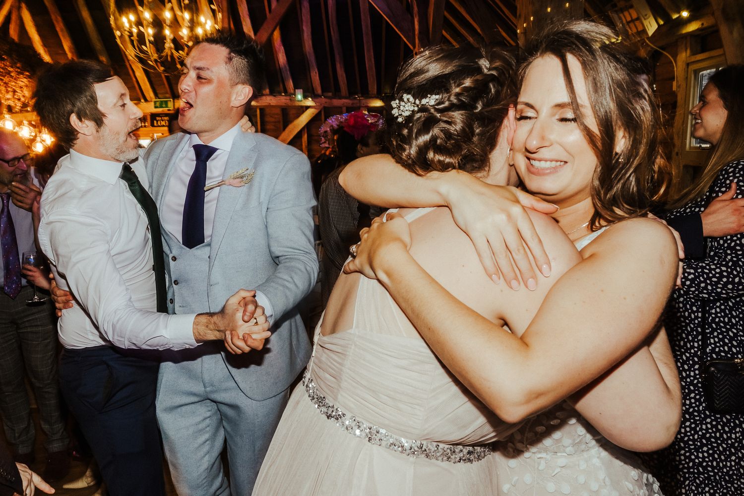 Wedding reception guests dancing and embracing under warm lighting.