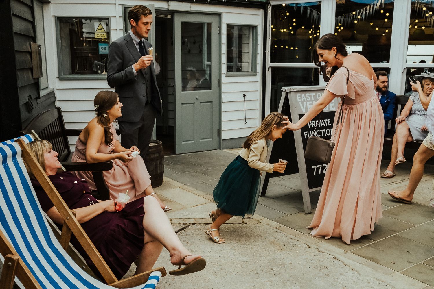 A group of wedding guests socializing and relaxing on deck chairs outside a building.