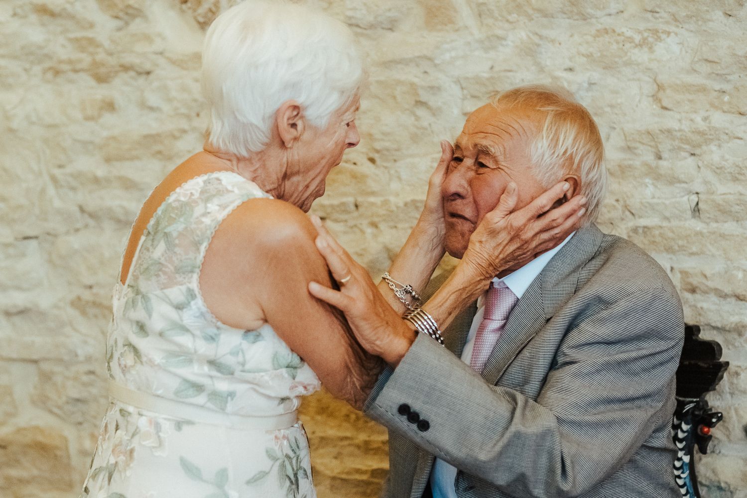 An emotional moment between an elderly couple at their wedding against a stone wall background.