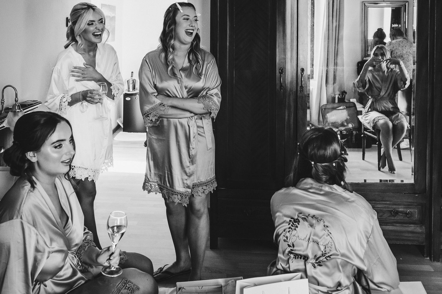 Black and white photo showing bridesmaids getting ready in silk robes on wedding morning.