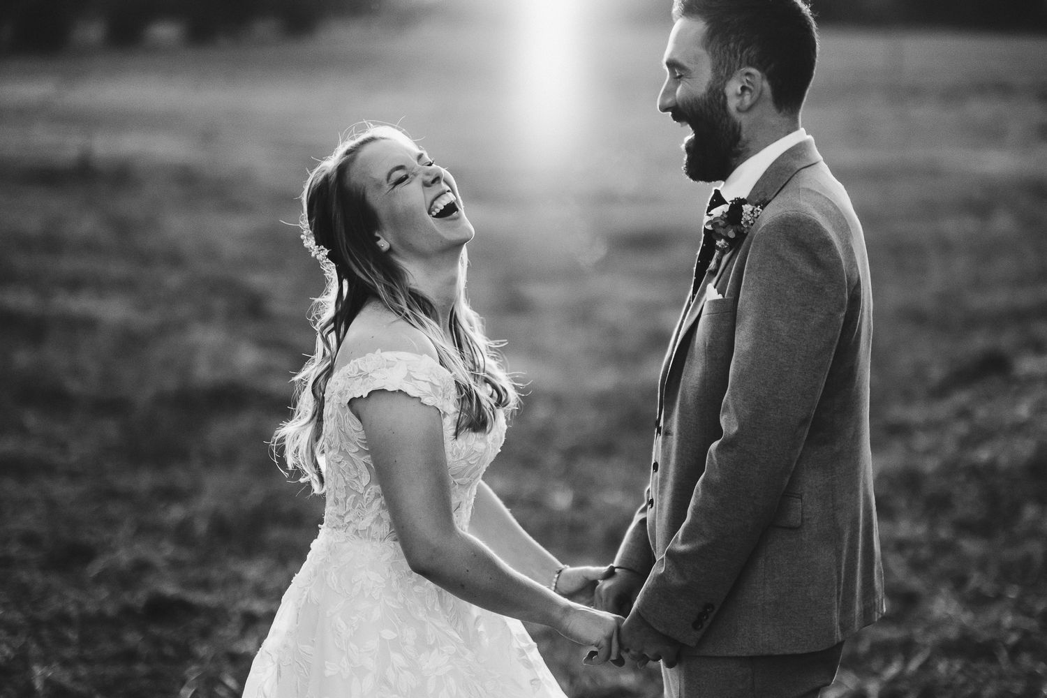 A joyful black and white moment of a couple laughing together during their outdoor wedding photoshoot.