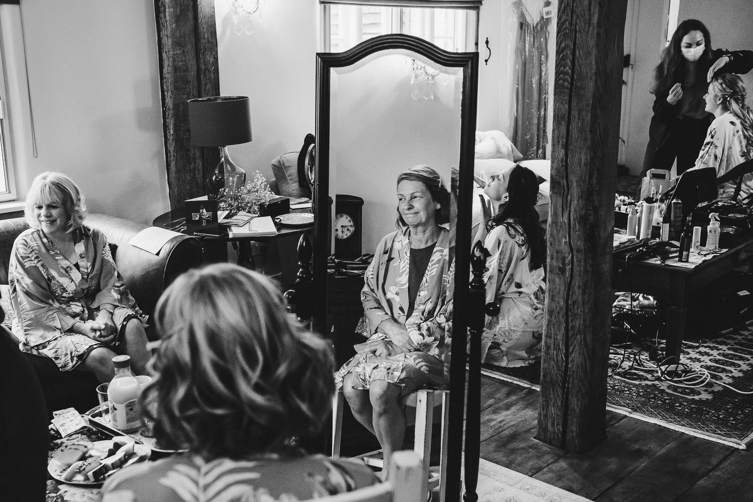 Wedding party getting ready in vintage-style room with wooden beams and mirrors.