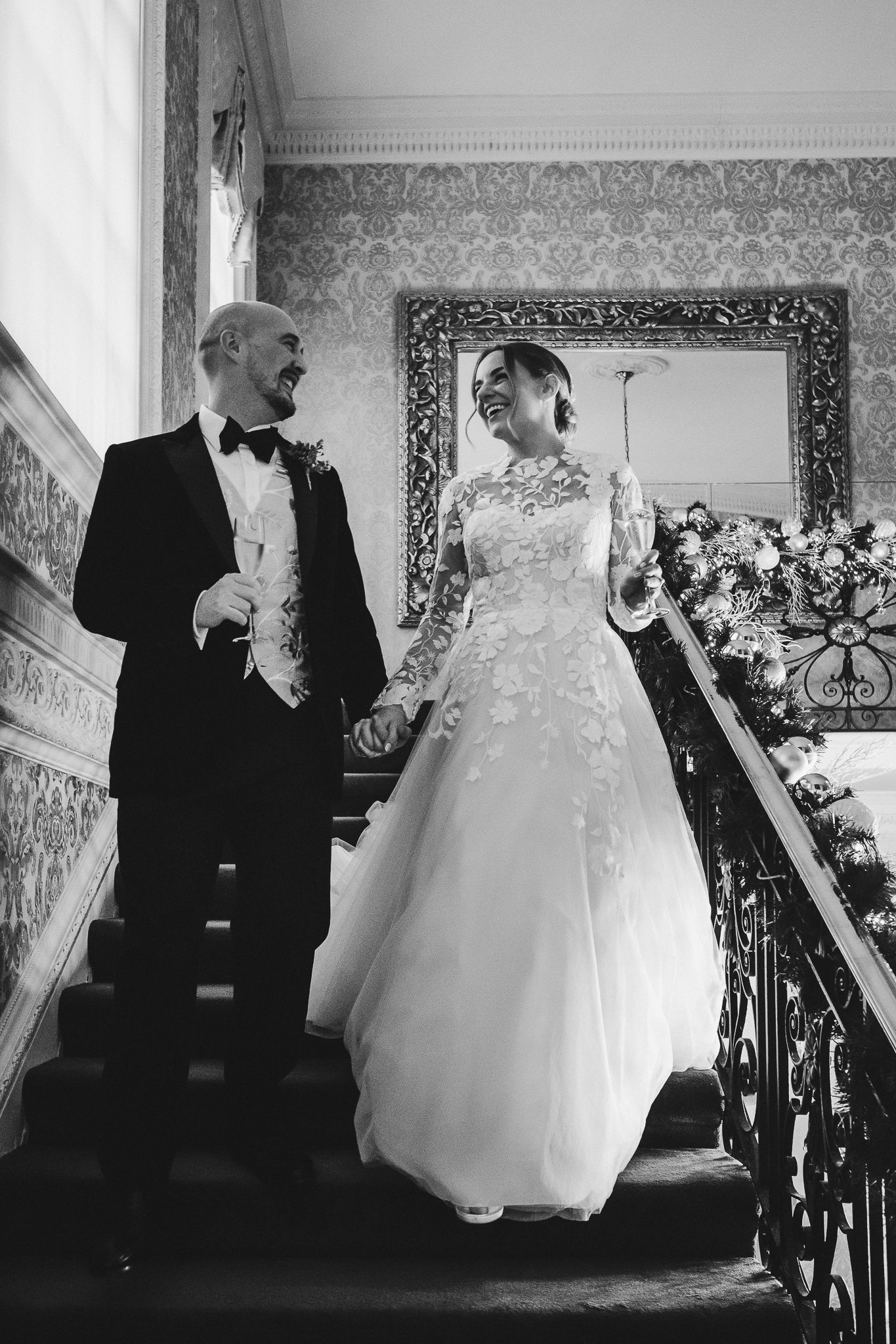 Bride and groom share intimate moment on grand staircase in black and white.