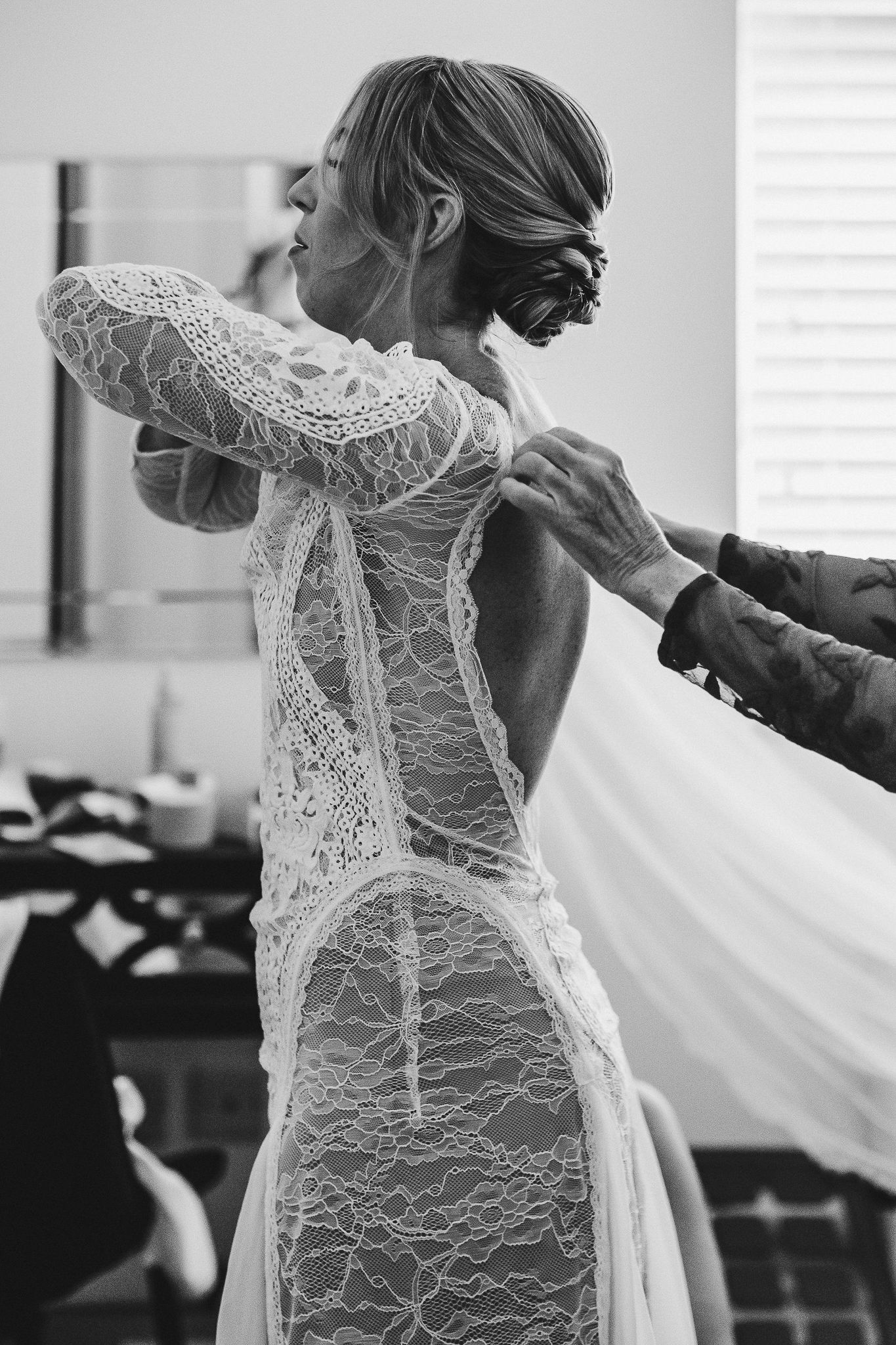 Close-up details of a delicate lace wedding dress being fitted, showing intricate patterns and buttons.