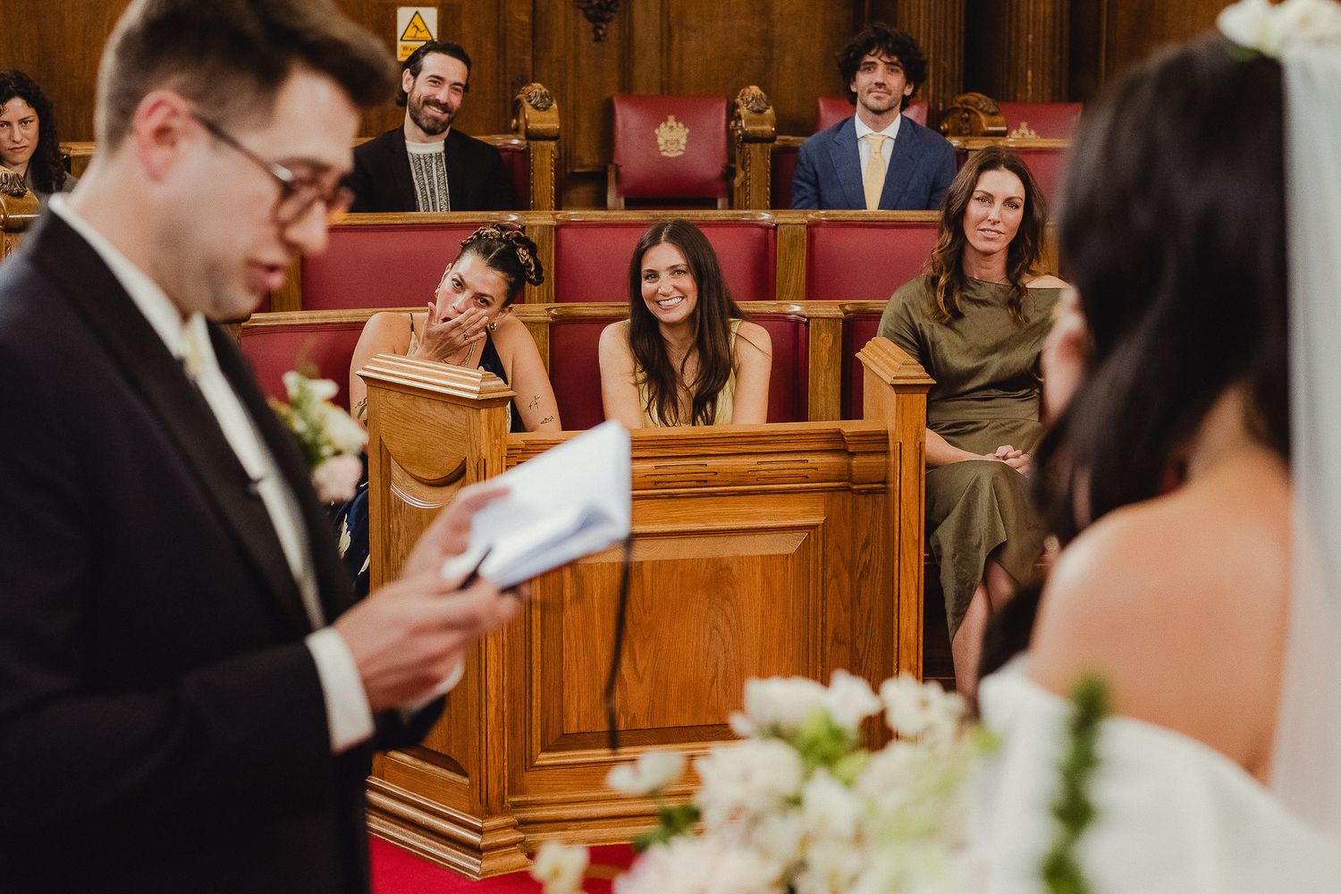 A groom reads vows during an intimate church wedding ceremony as guests watch from wooden pews.