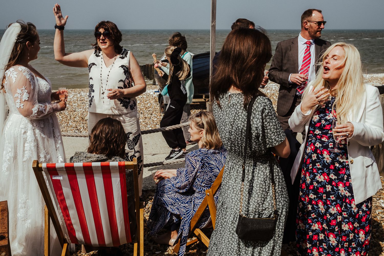 Guests enjoying drinks and conversation at a beachside wedding reception with striped chairs.