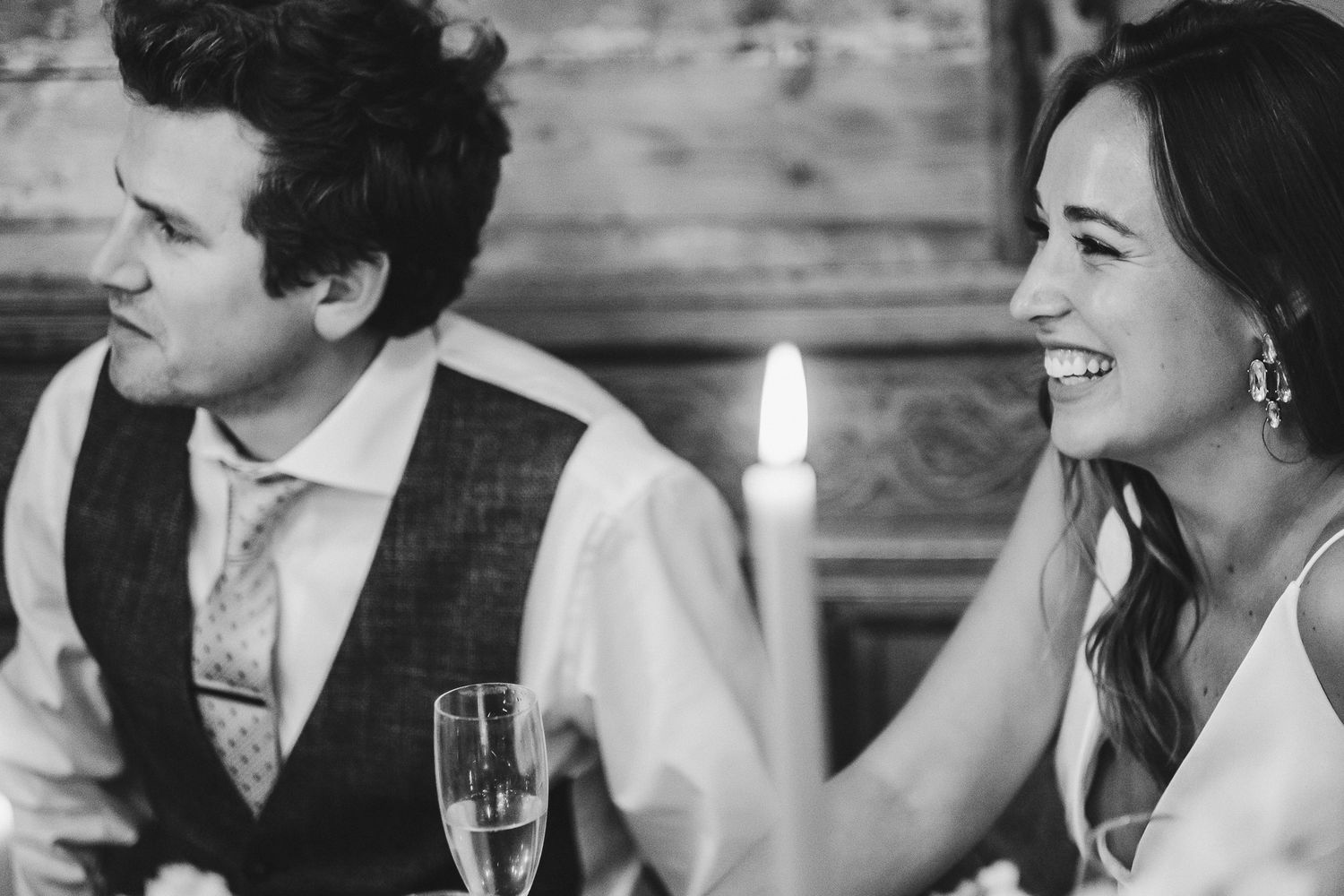 Black and white candid moment of a couple laughing during wedding reception.