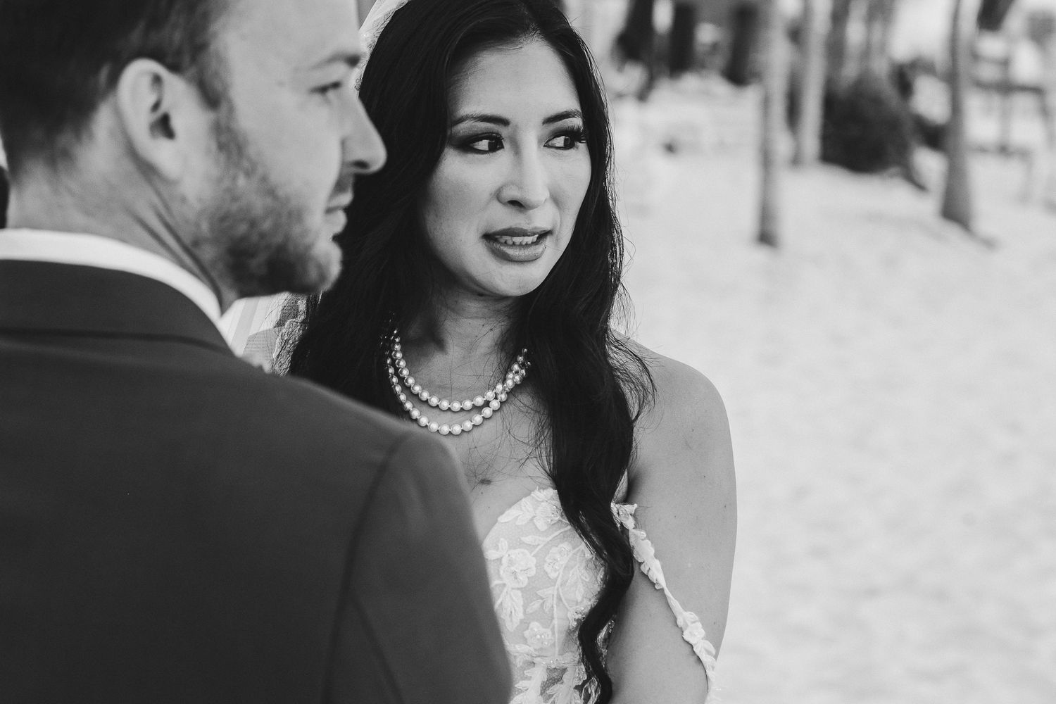 Close up black and white portrait of a bride in a lace dress and pearl necklace.