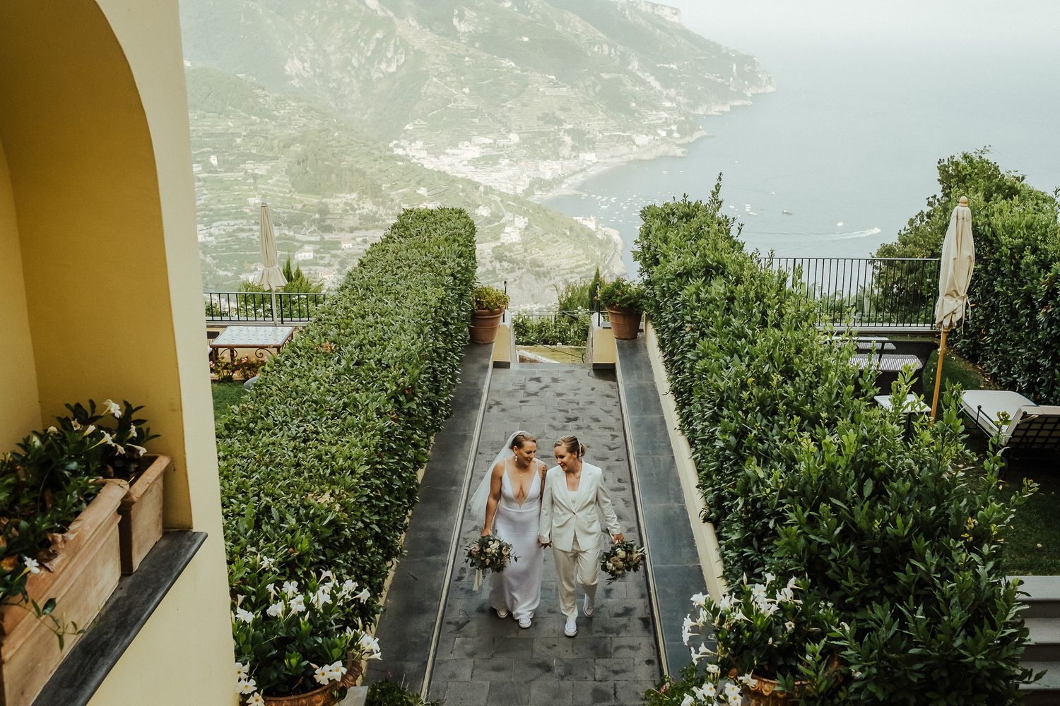 Aerial view of a couple walking down a path with Mediterranean coastal views.