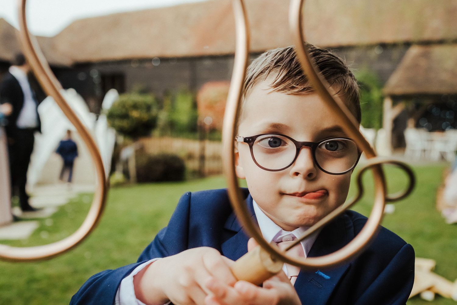 Child wearing glasses smiles while sitting outdoors in natural lighting.