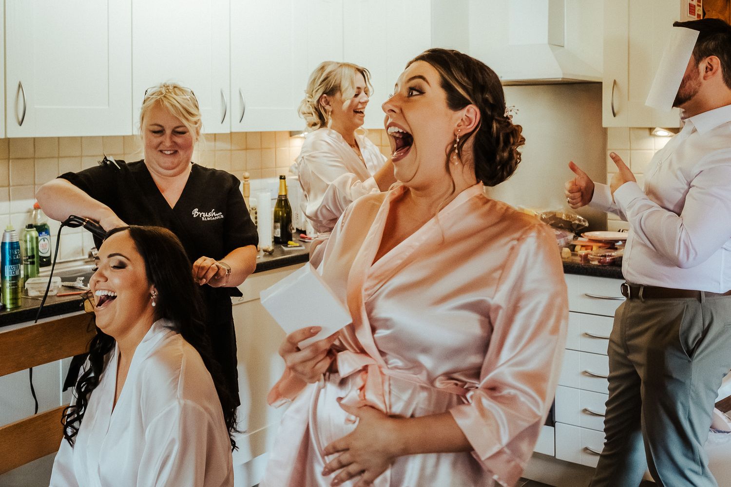 Group getting ready in kitchen wearing robes with excited expressions during wedding preparations.