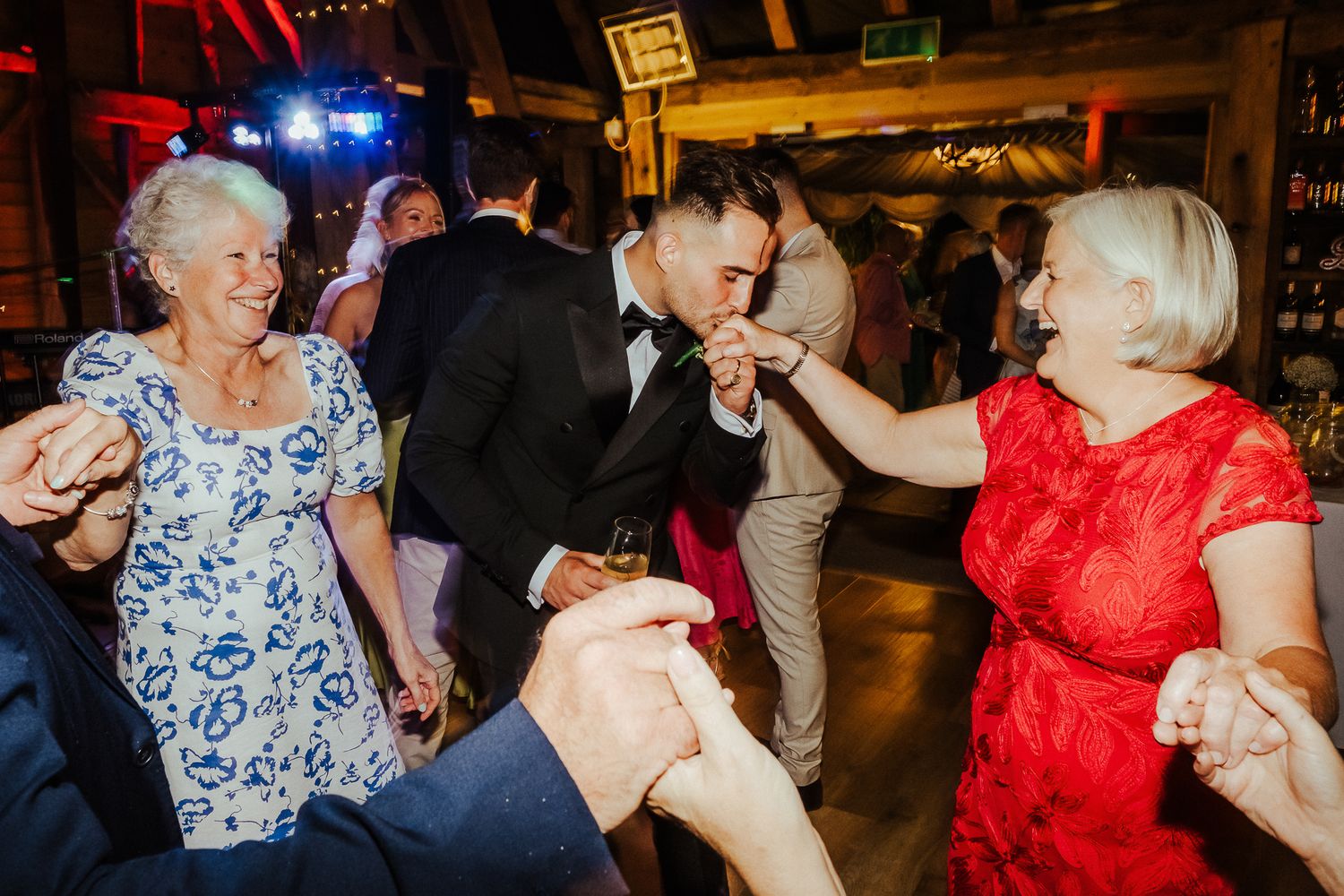 Guests dancing and celebrating at a vibrant wedding reception with colorful lighting.