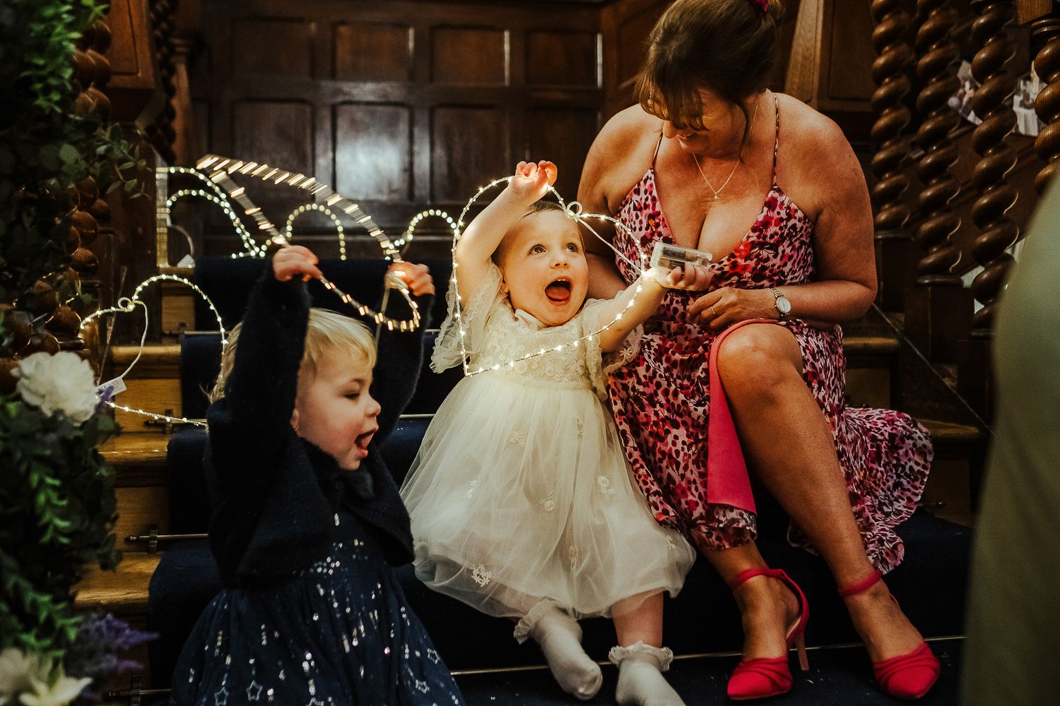 Wedding guests sitting on wooden steps with festive Christmas lights in the background.