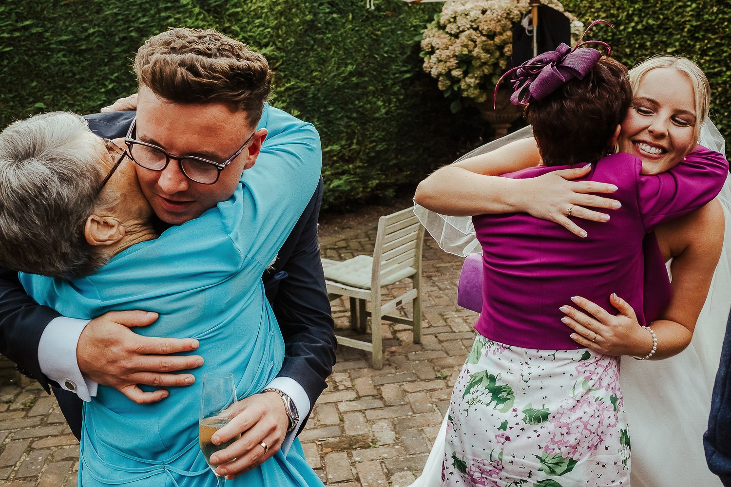 Wedding guests embrace warmly in an outdoor garden setting with festive joyful emotions.
