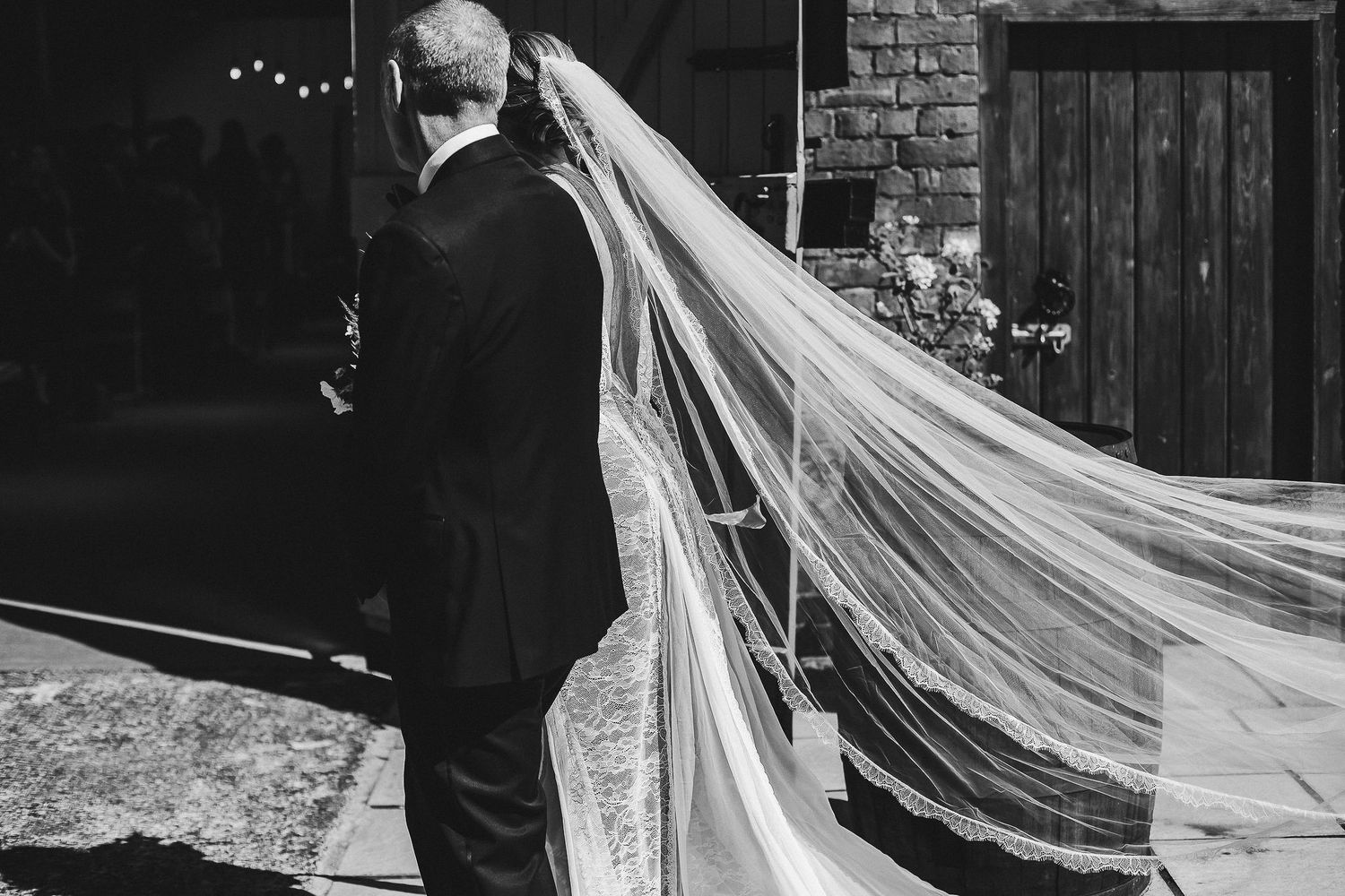 Long flowing wedding veil trailing behind couple in black and white photography.