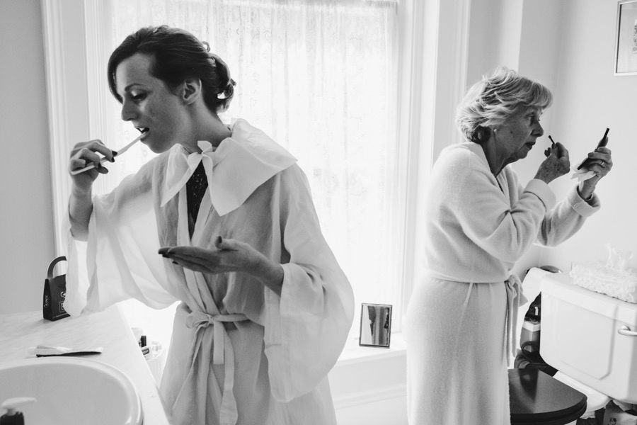 Morning wedding preparations in white robes by window light in classic black and white.