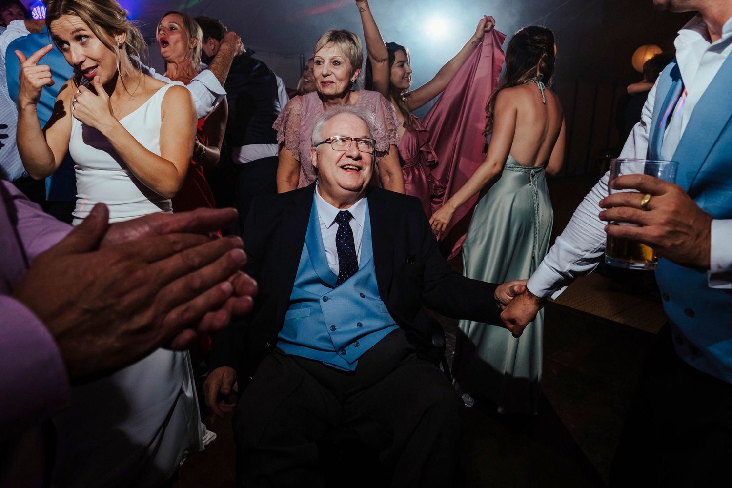 Wedding guests dance and celebrate on a dimly lit dance floor during the reception.