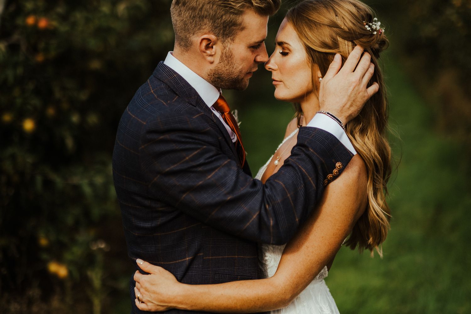 A romantic wedding portrait showing tender embrace against a natural backdrop.