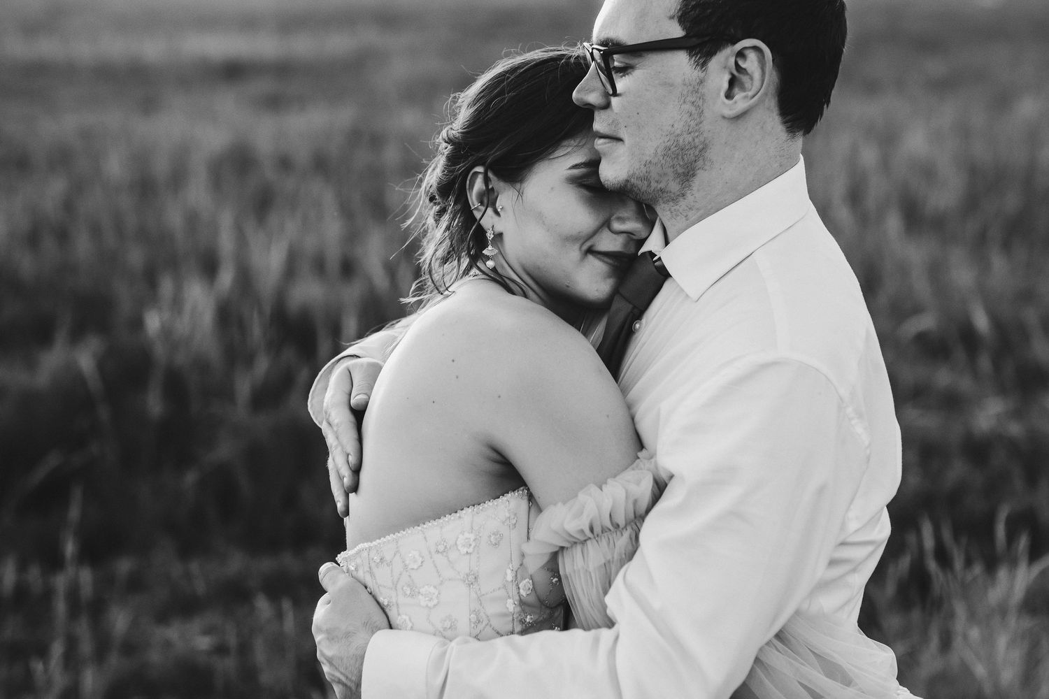 An intimate black and white portrait of a couple embracing in formal wear.