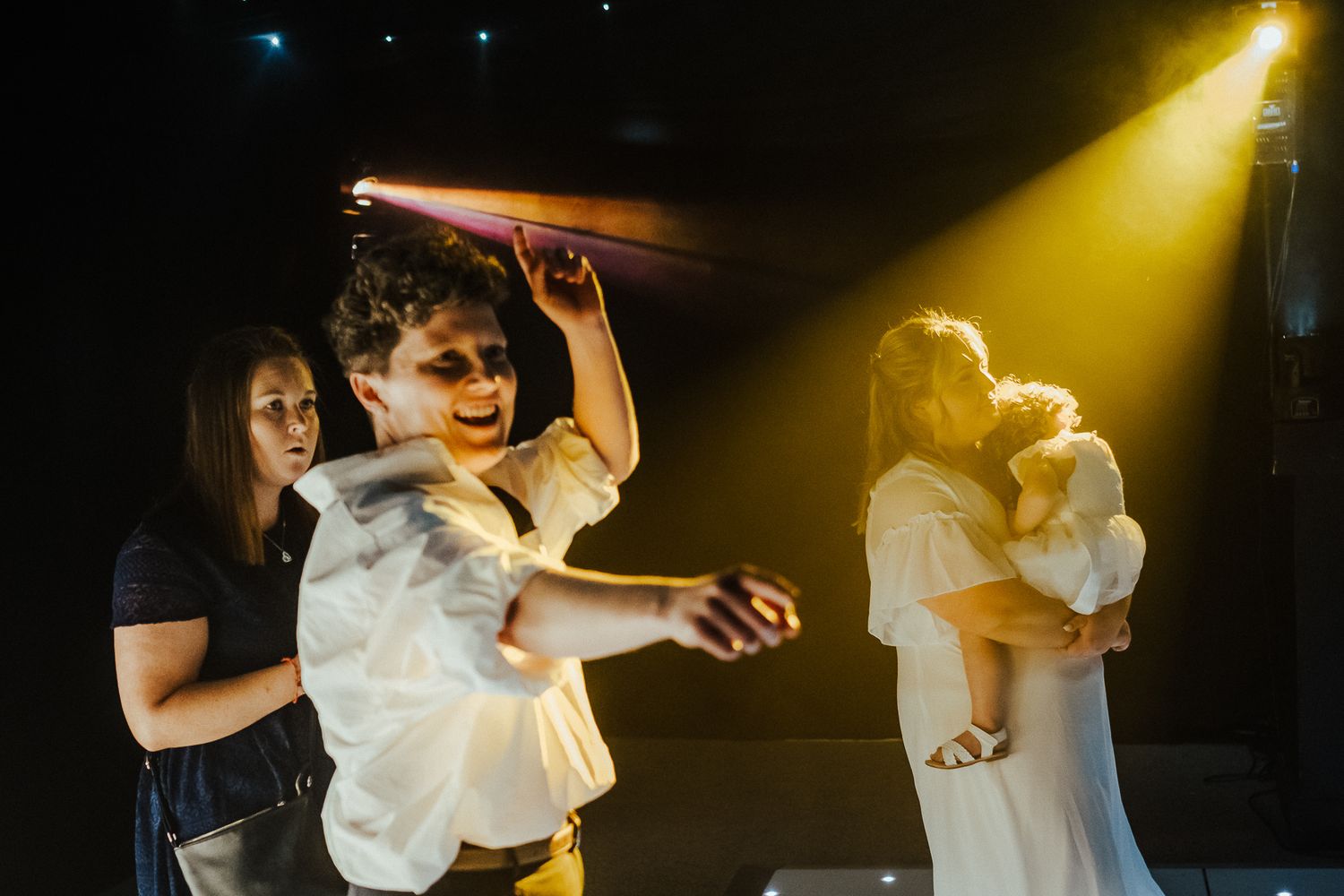 Wedding celebration on dance floor with dramatic yellow spotlight illumination.