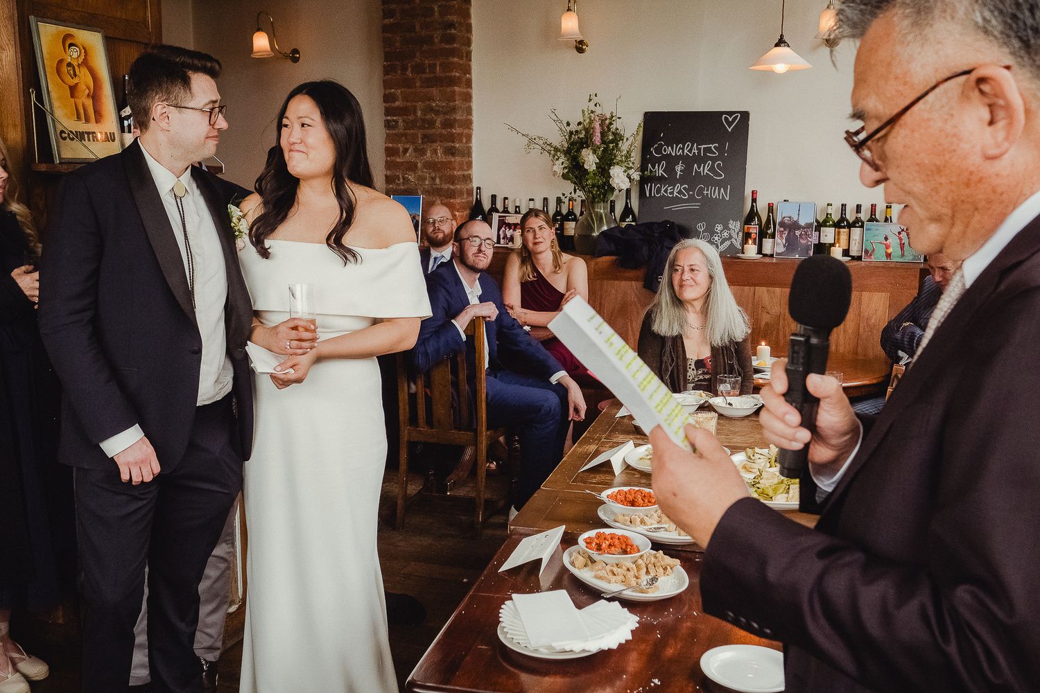 Wedding guests enjoy a formal reception celebration while dining at tables in an elegant brick-walled restaurant space.