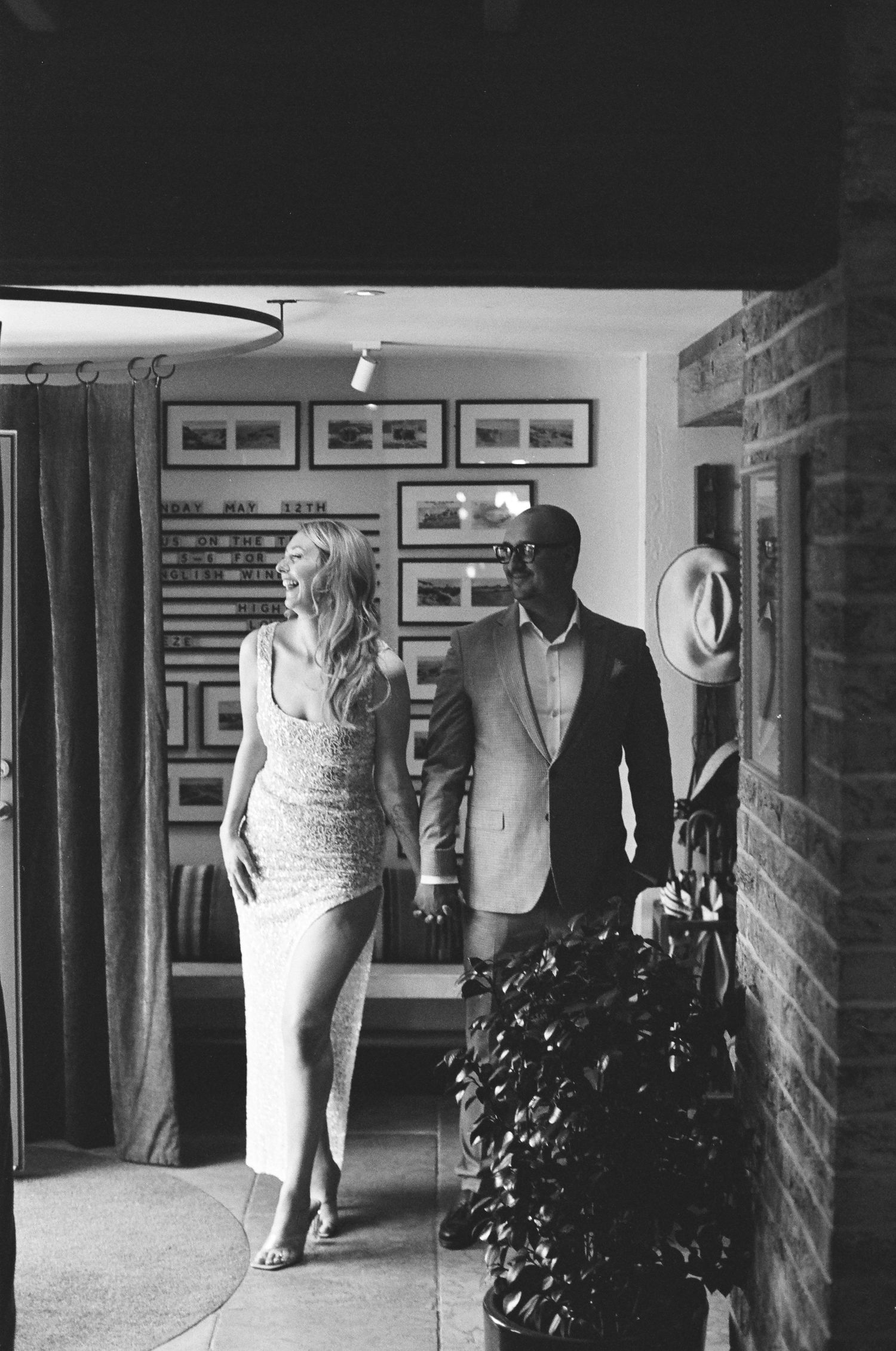 A black and white gallery hallway displays mannequins in elegant dresses against a brick wall.