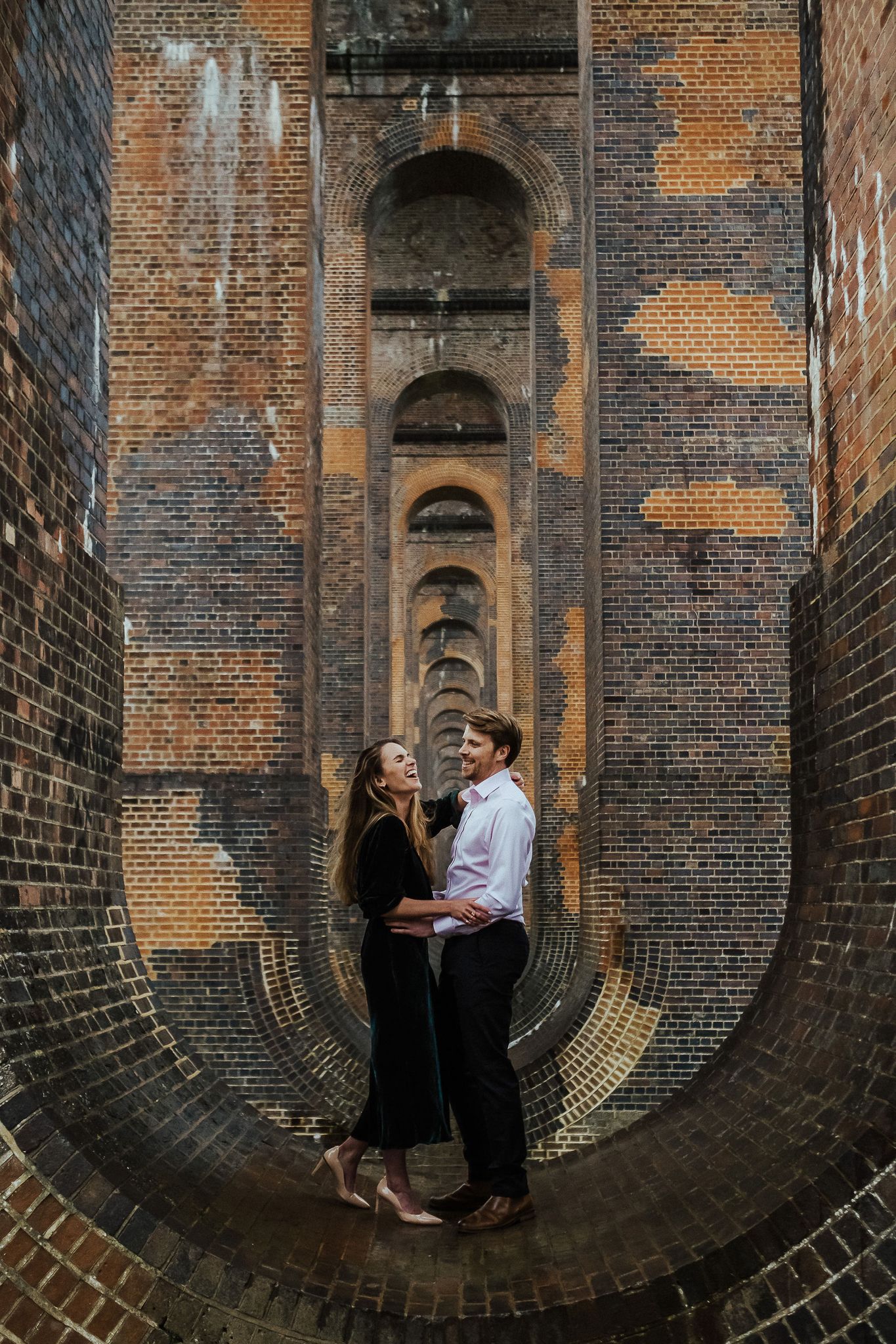 Intimate portrait of a couple embracing in an industrial brick archway.