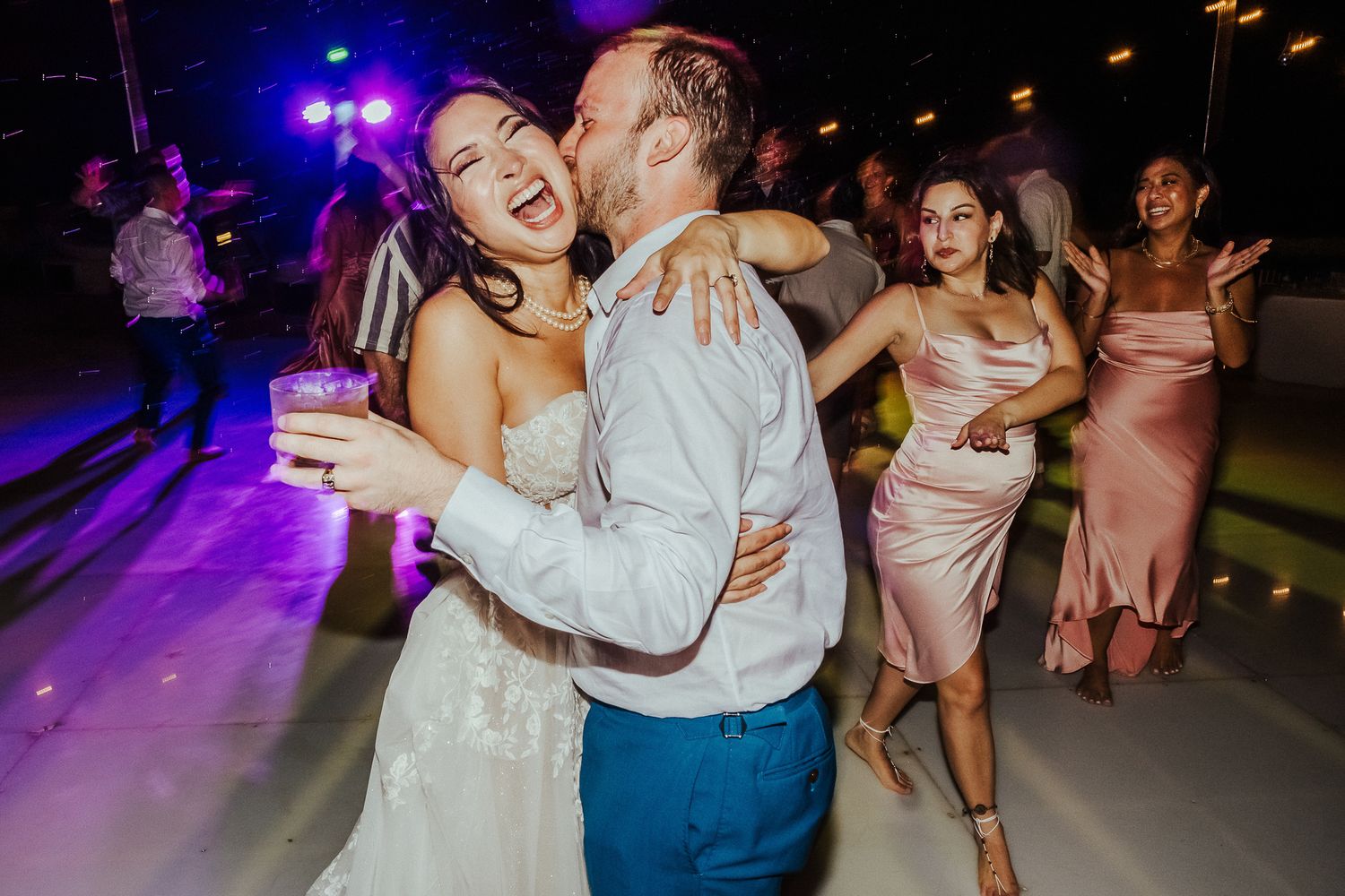 Couples dancing together on a colorful illuminated dance floor at a wedding reception.