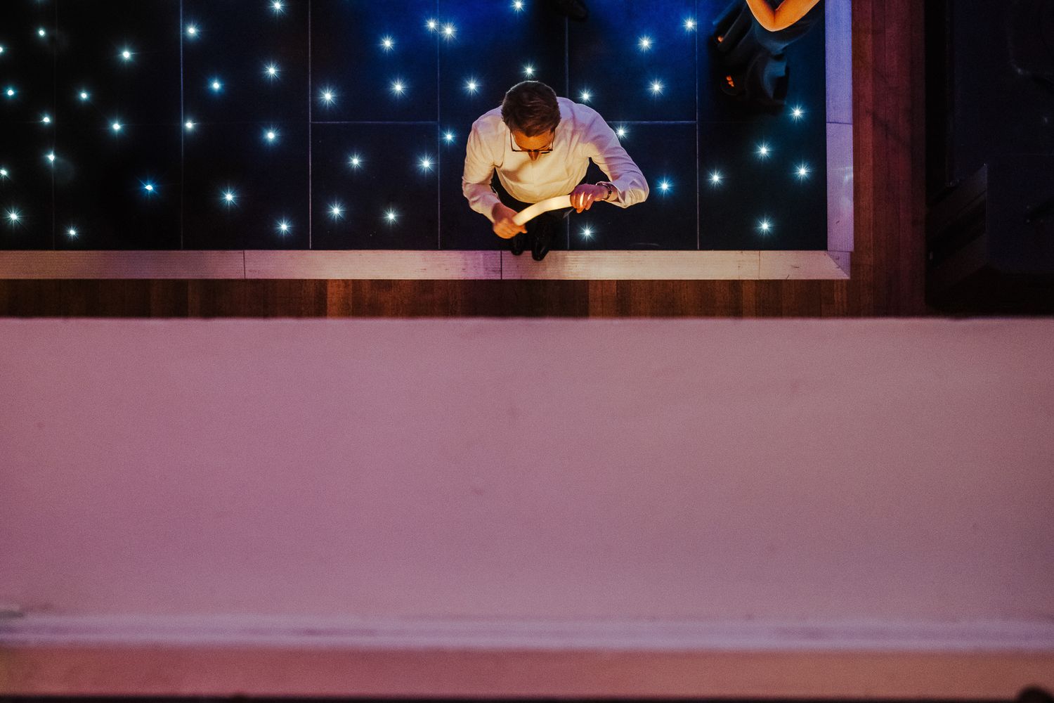 A silhouetted figure bending down against a backdrop of twinkling blue lights at night.