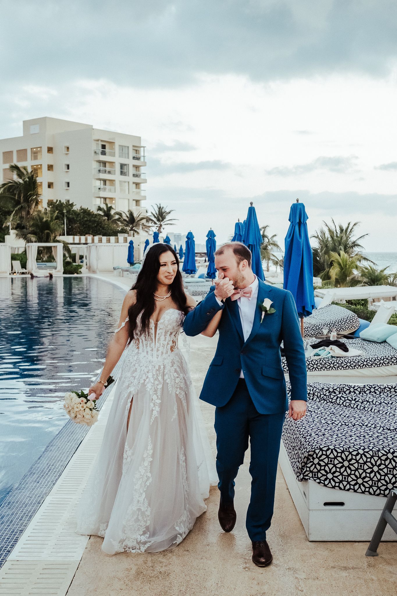 Happy newlyweds walk along luxurious poolside at tropical resort.