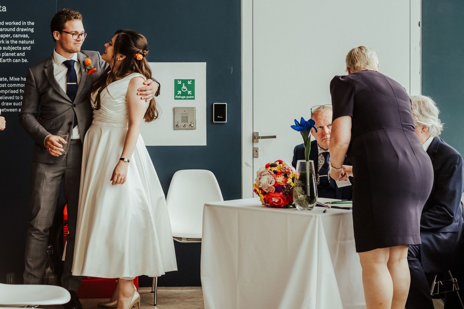 Couple signs marriage documents at table while officiant assists during reception.