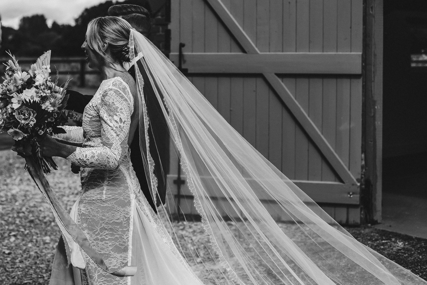 Wedding veil flowing in breeze against rustic wooden backdrop.