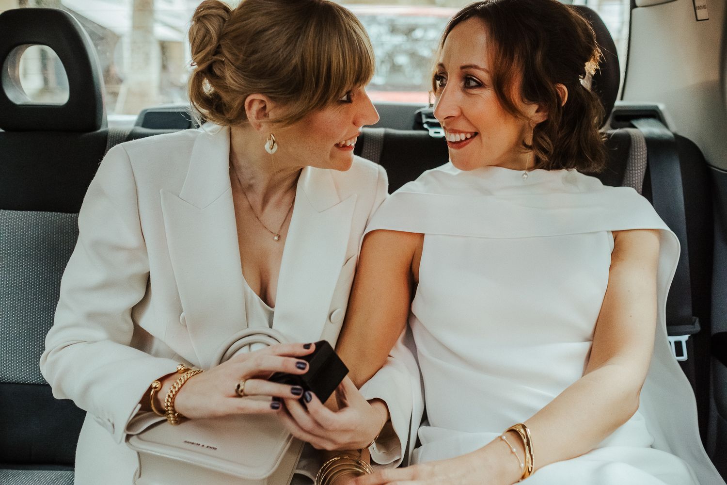 Two people in white outfits sharing a joyful moment together in the back of a car.