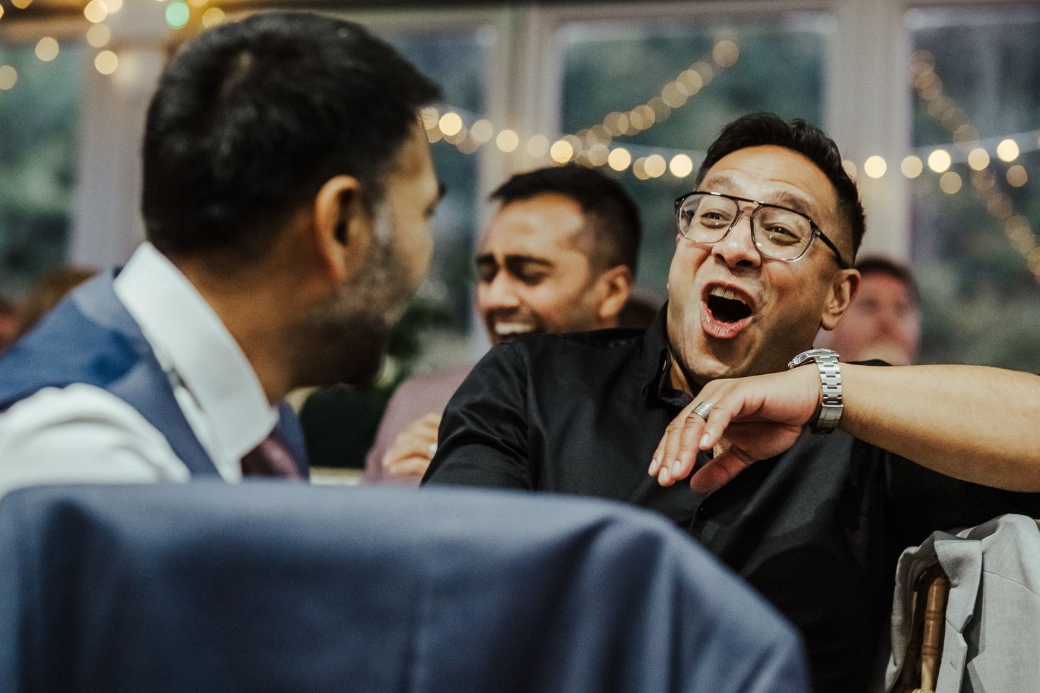 A group of friends share a candid moment of laughter and joy at a social gathering under string lights.