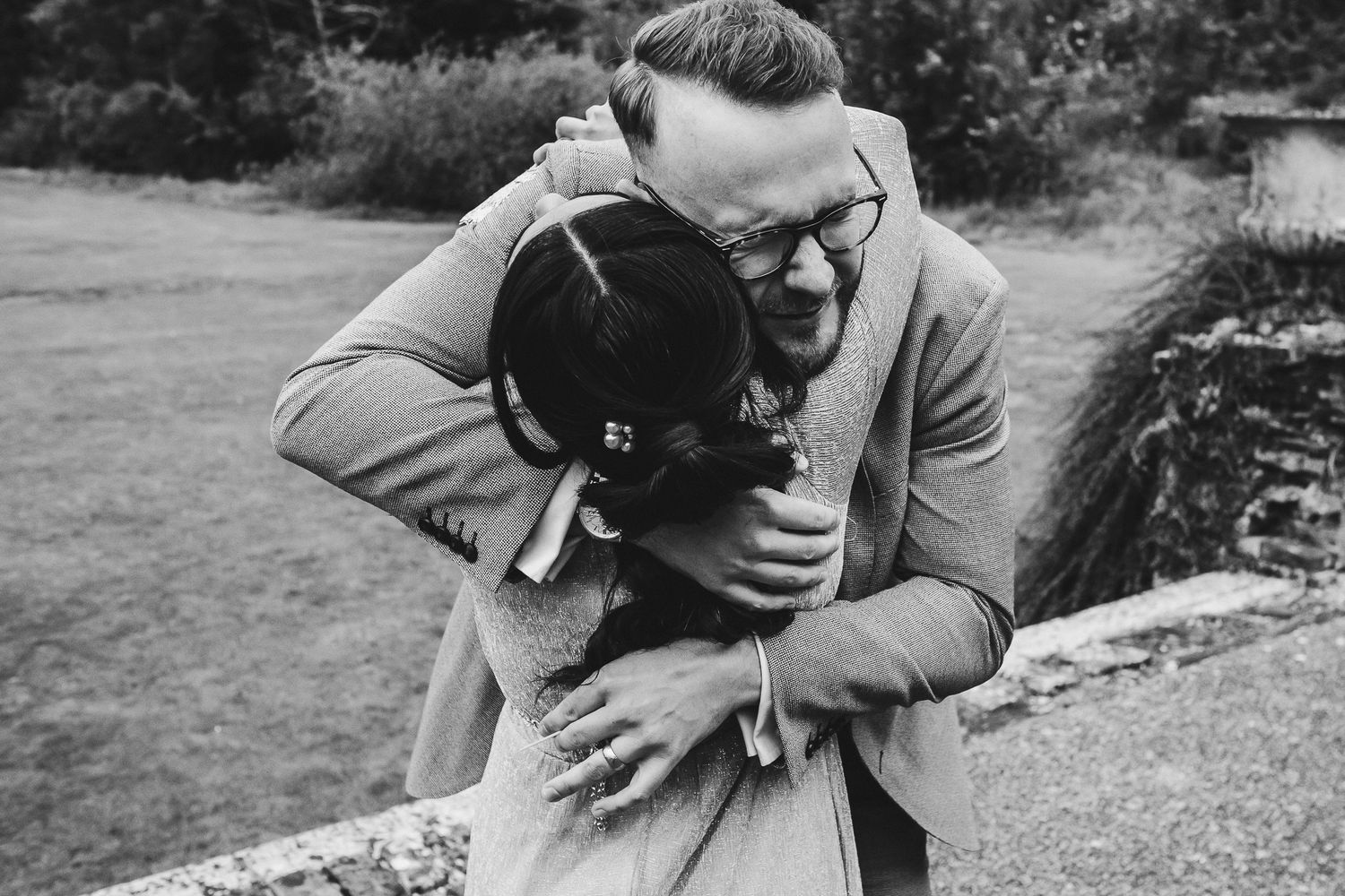 Two joyful people embrace with laughter and affection outdoors in a black and white photograph.