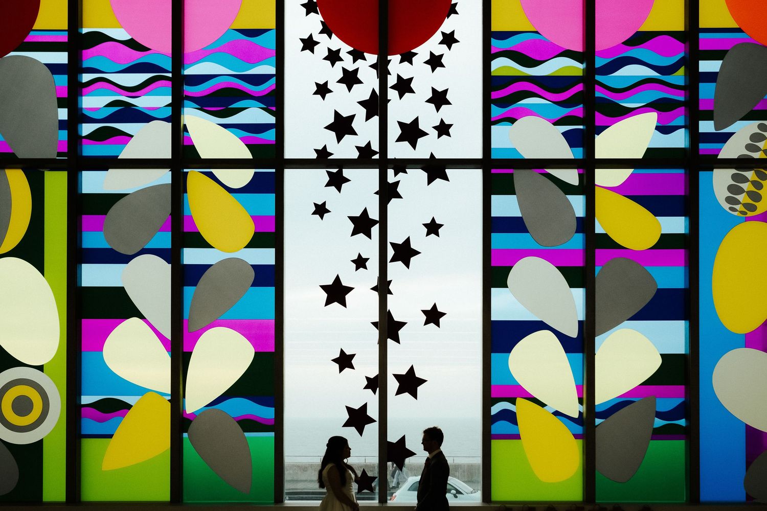 Colorful stained glass window with star patterns creates artistic silhouettes.