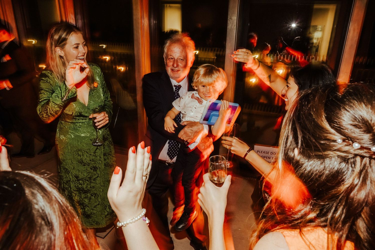 Wedding guests laugh and celebrate during evening reception with warm lighting.