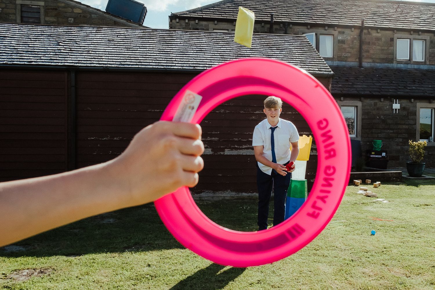 Creative wedding photo framing groom through pink ring toy in garden setting.
