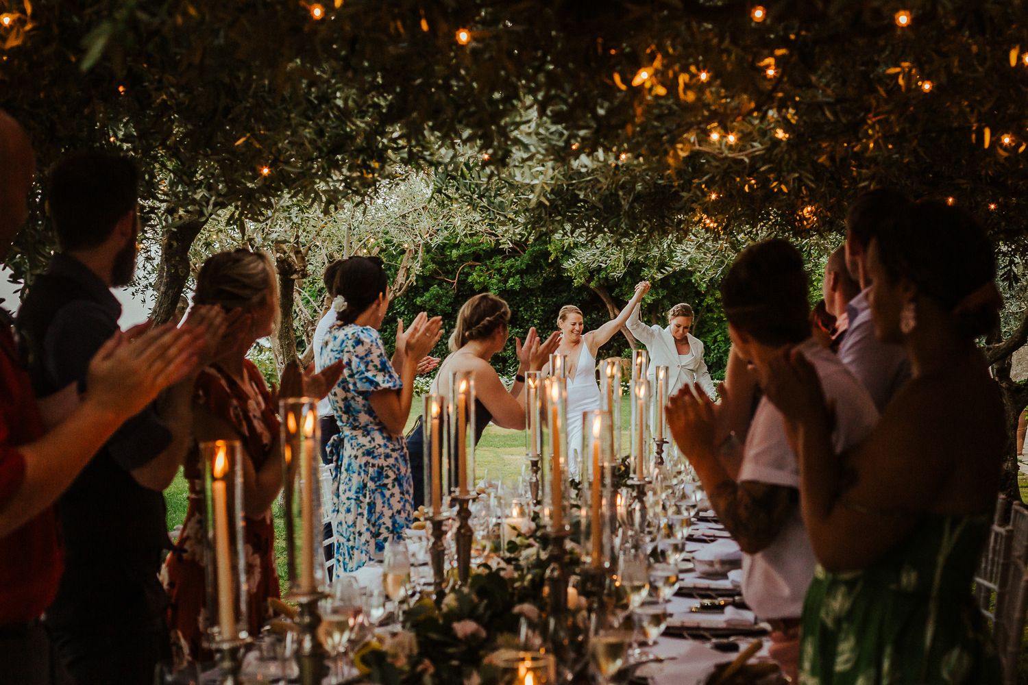 Outdoor wedding reception under twinkling lights and tree canopy at dusk.