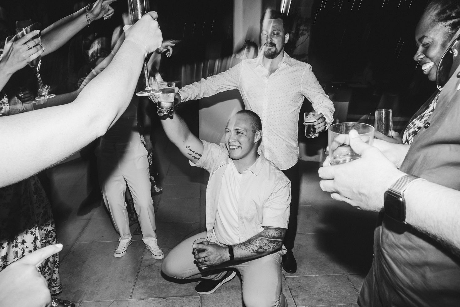 Energetic party guests dancing and celebrating on a dance floor in black and white.