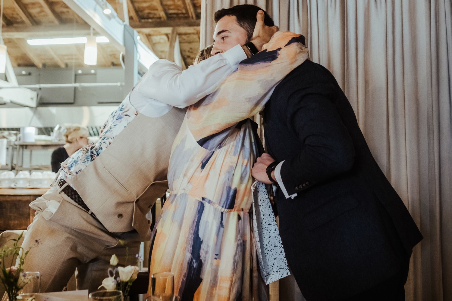 Candid celebration showing joyful embrace between wedding attendees at reception venue.