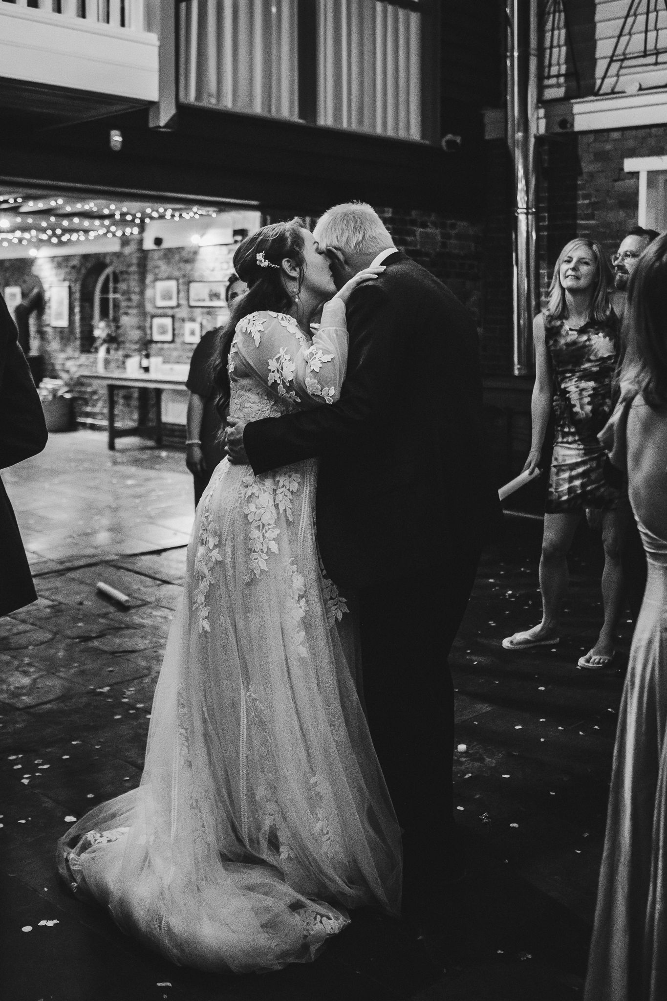 A romantic black and white photo of newlyweds sharing their first dance in a venue with string lights.