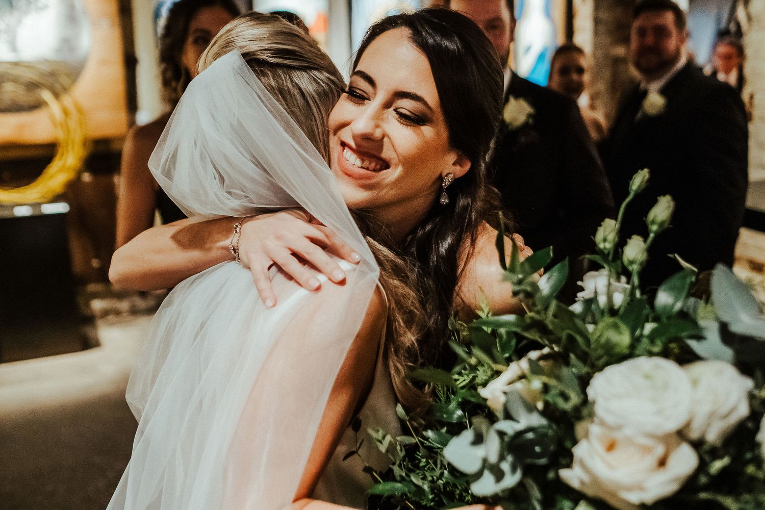 Two people share a joyful embrace during a wedding celebration surrounded by floral arrangements.
