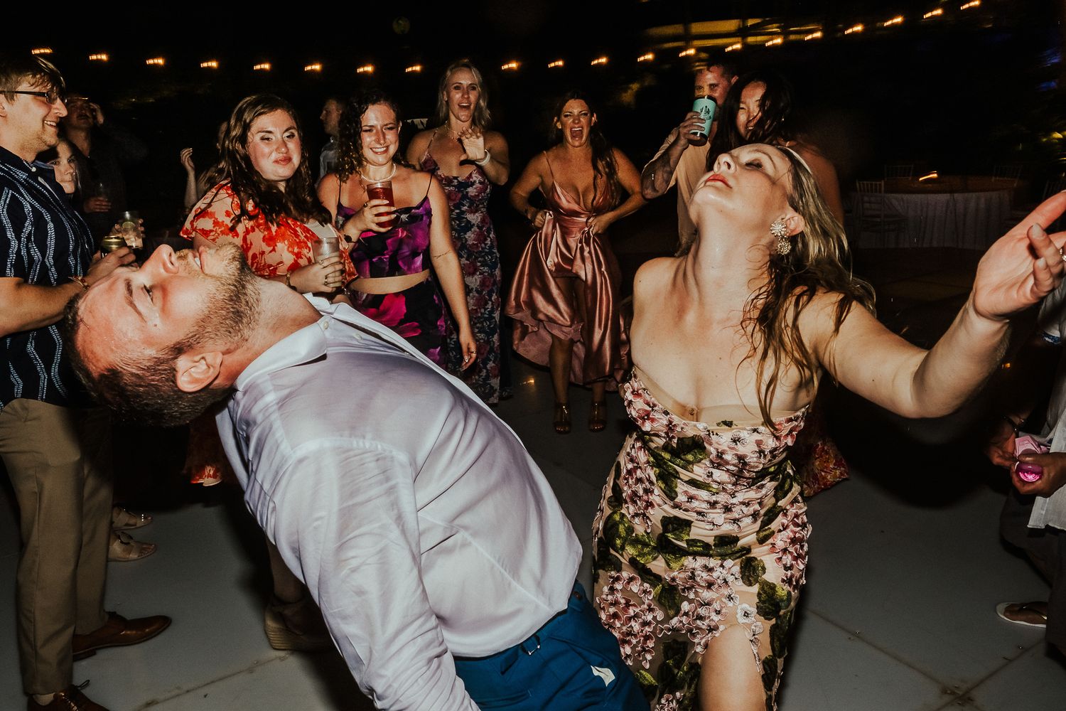 Wedding guests dance enthusiastically under string lights at an outdoor reception.