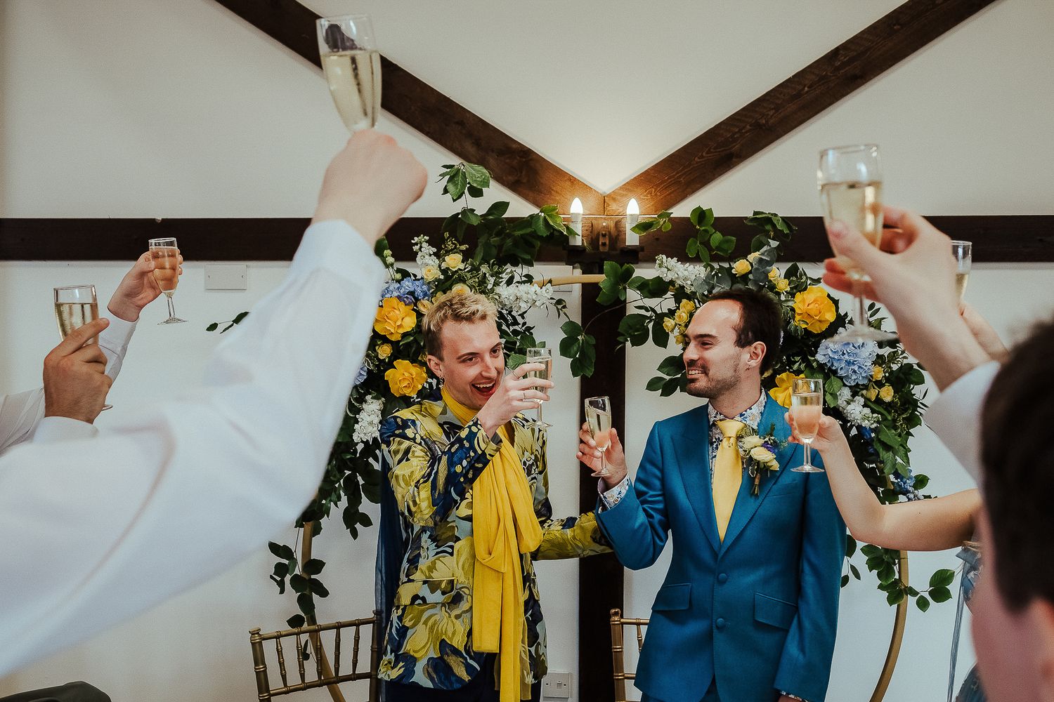 Wedding celebration with guests toasting under wooden beams and floral decorations.