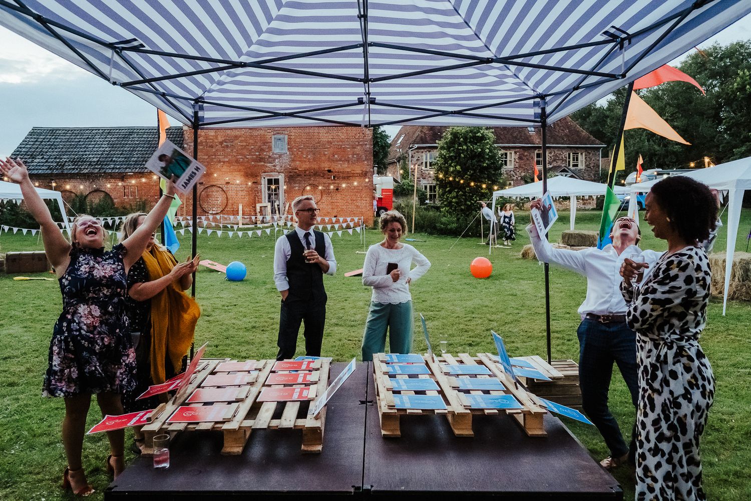 Wedding guests play lawn games under a striped tent at an outdoor reception.