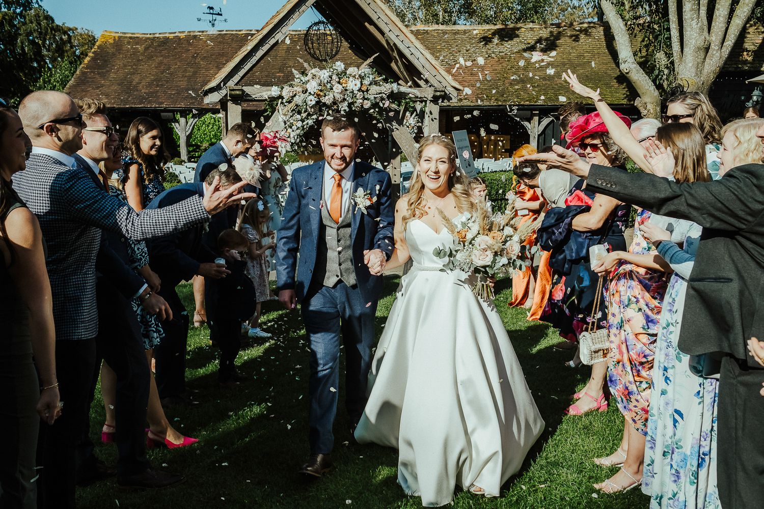 Newlyweds celebrate with guests throwing confetti in garden setting.